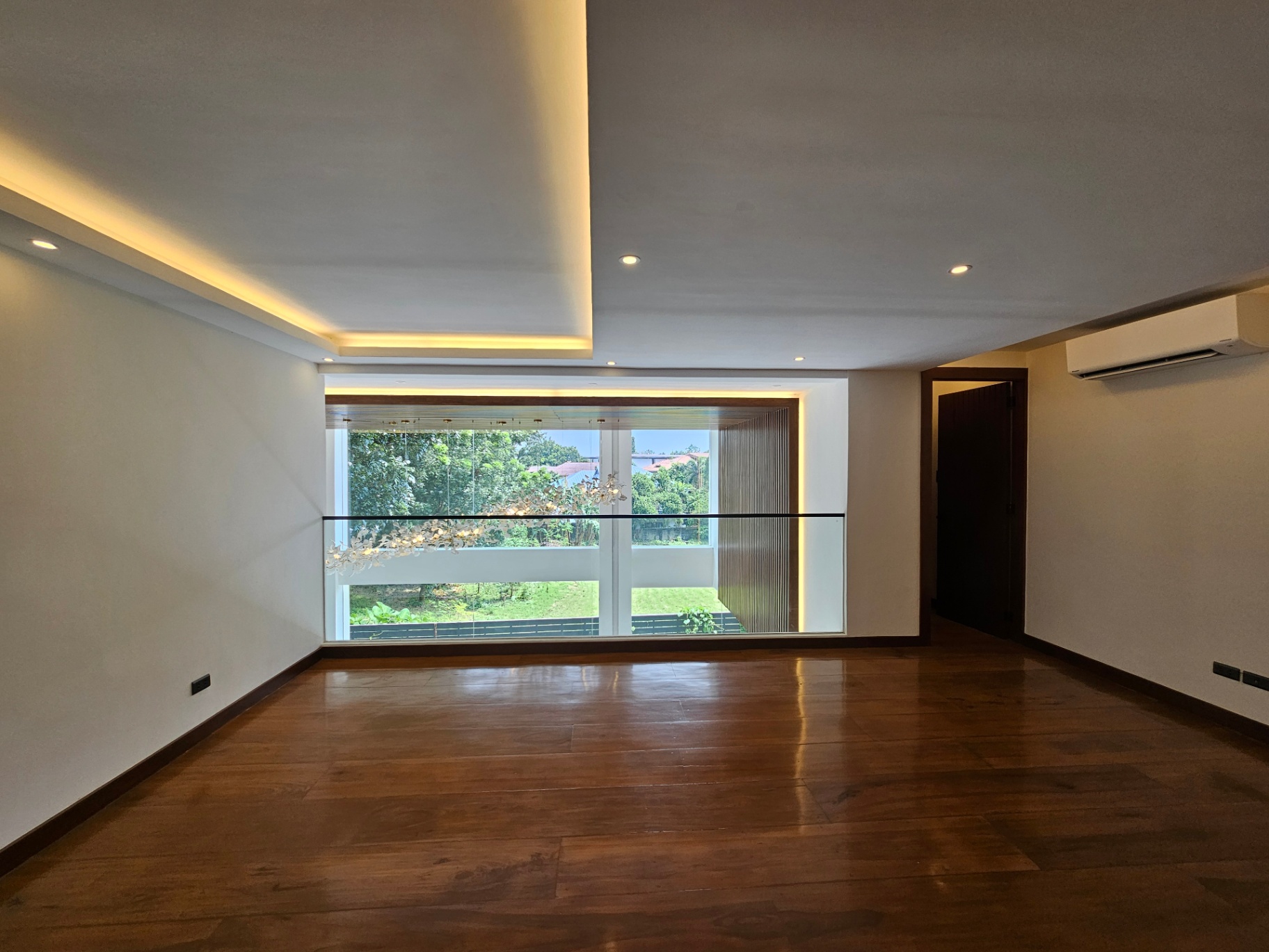 Upper floor bedroom with warm wood floors, cove lighting, and garden view window