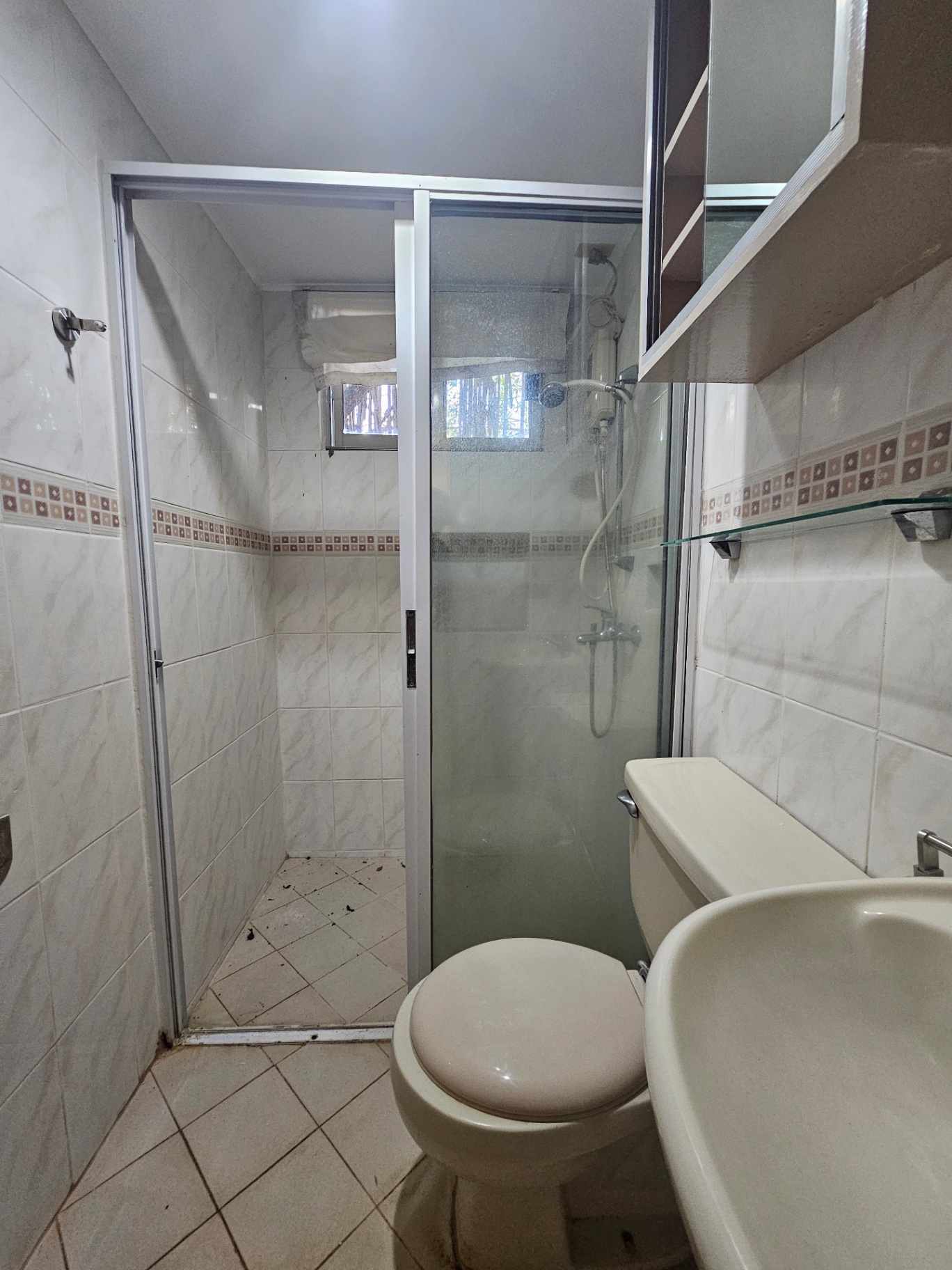 Bathroom with white marble tiles, glass shower enclosure, and vanity shelf