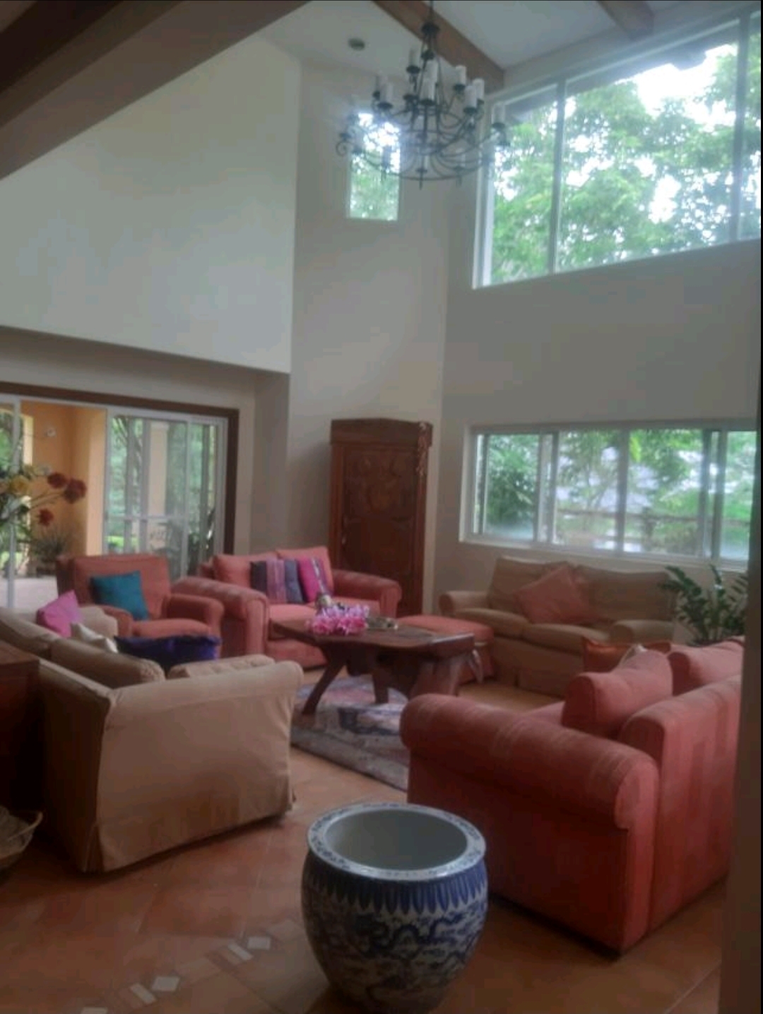Double-height living room with narra ceiling beams, wrought-iron chandelier and floor-to-ceiling windows