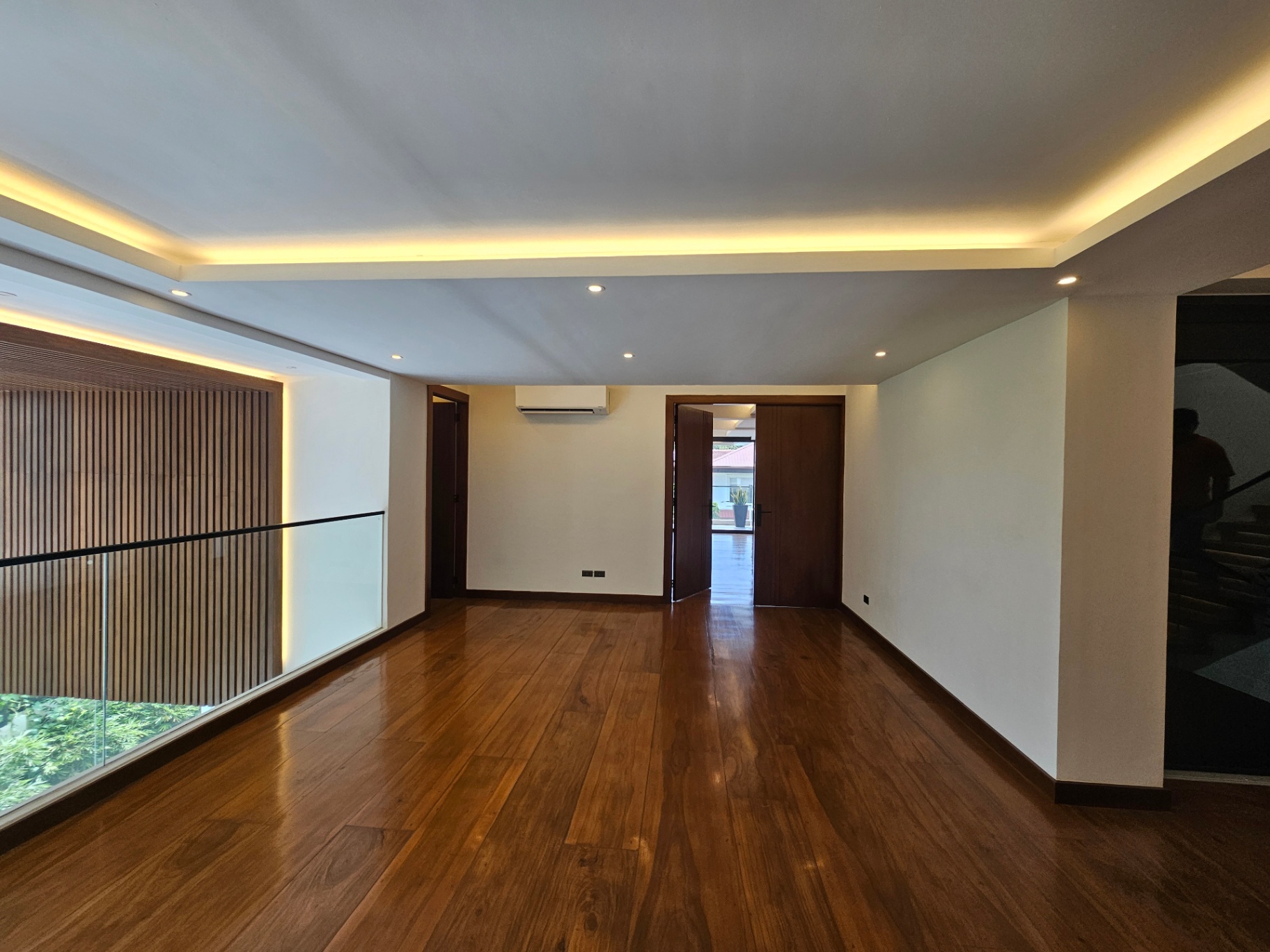 Upper floor hallway with rich wood floors, cove lighting, and staircase view
