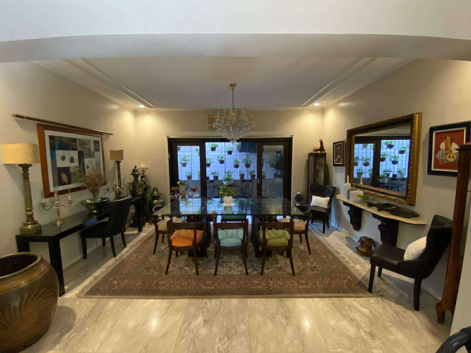 Formal dining room with glass table, chandelier, and antique consoles