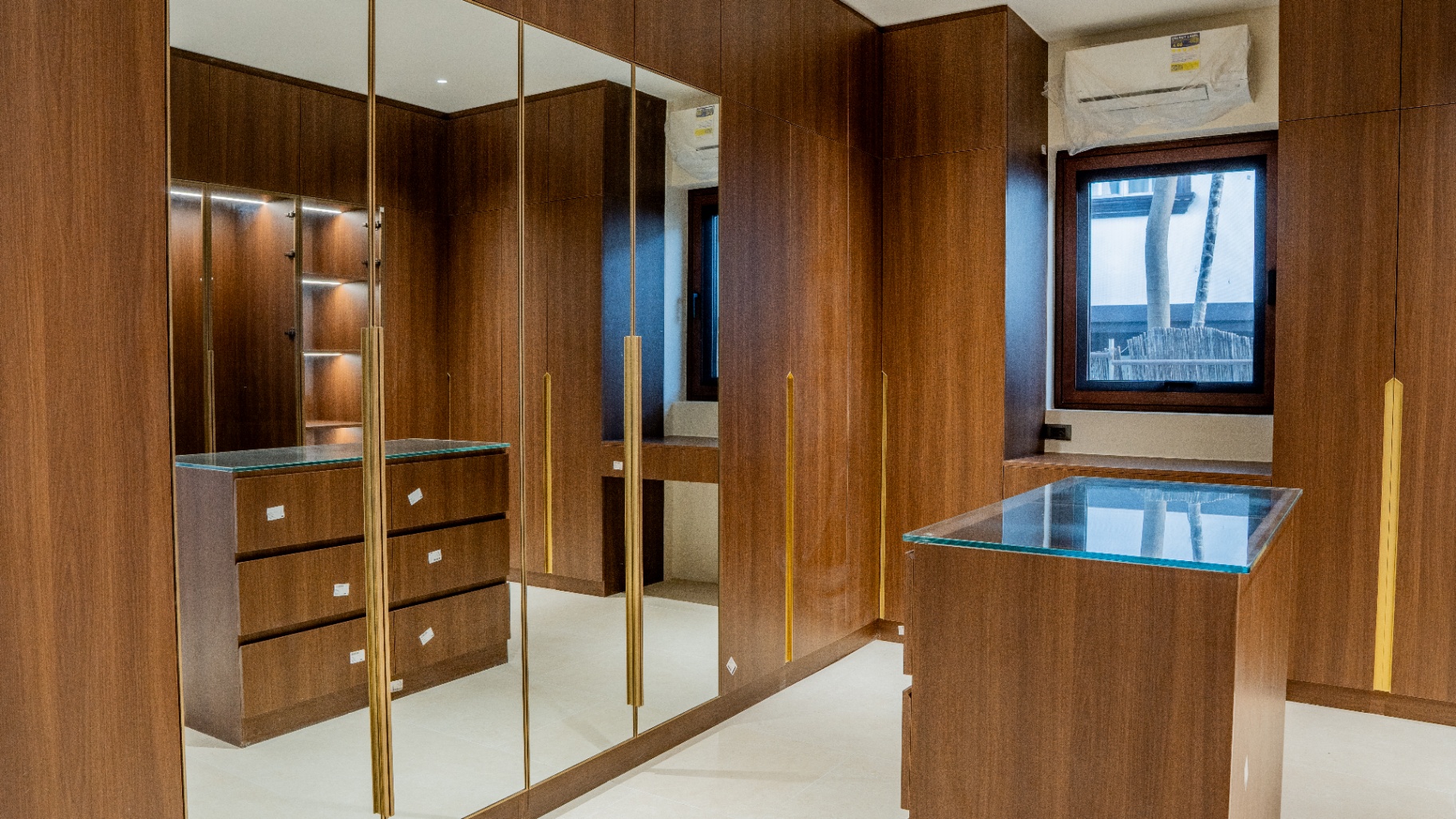 Large walk-in closet in wood veneer with mirrored doors and glass-top island