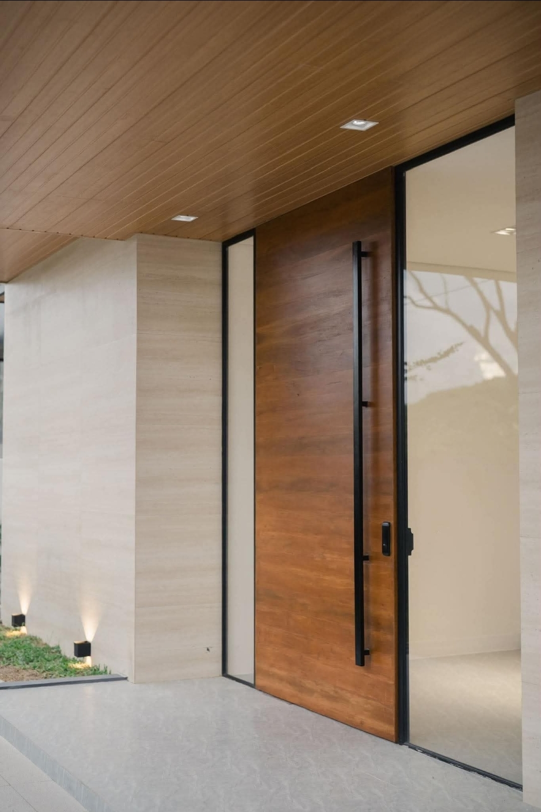 Timber pivot entry door under a wood-lined soffit with travertine walls