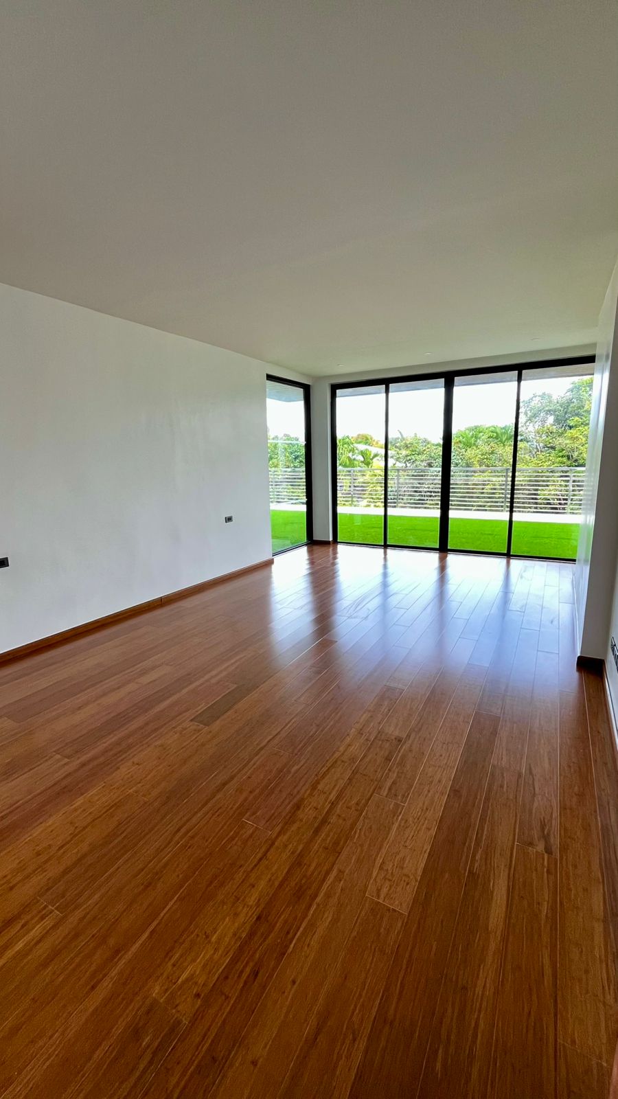 Family room with warm oak floors framed by full-height glass overlooking the lawn and pool