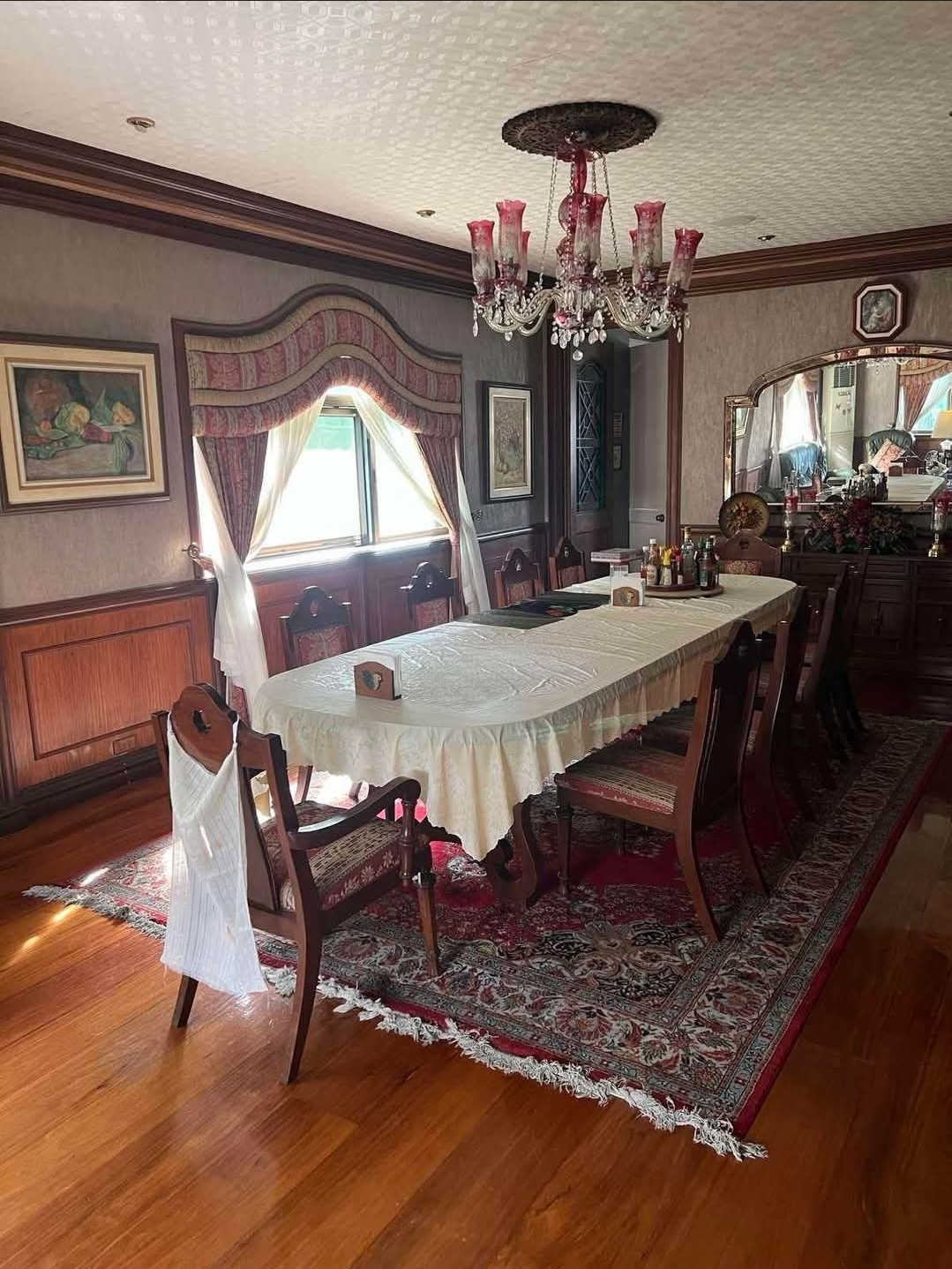 Formal dining room with a long table, crystal chandelier, and wood-paneled walls