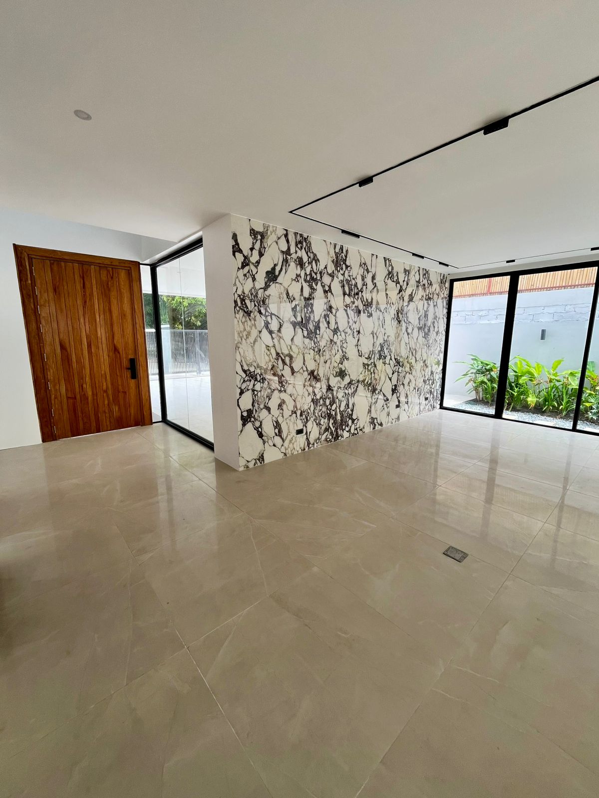 Grand foyer with statement book-matched marble feature wall, solid wood entry door, and floor-to-ceiling glass