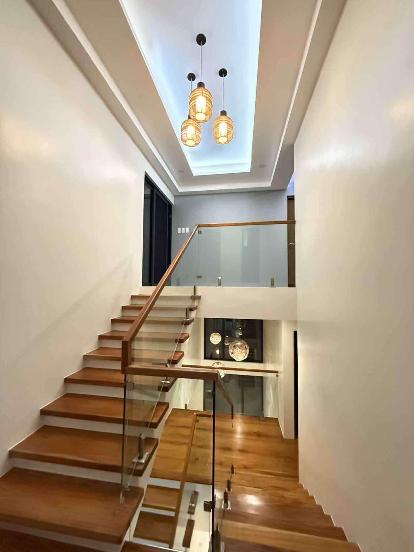 Solid wood staircase with glass balustrade and woven pendant lights