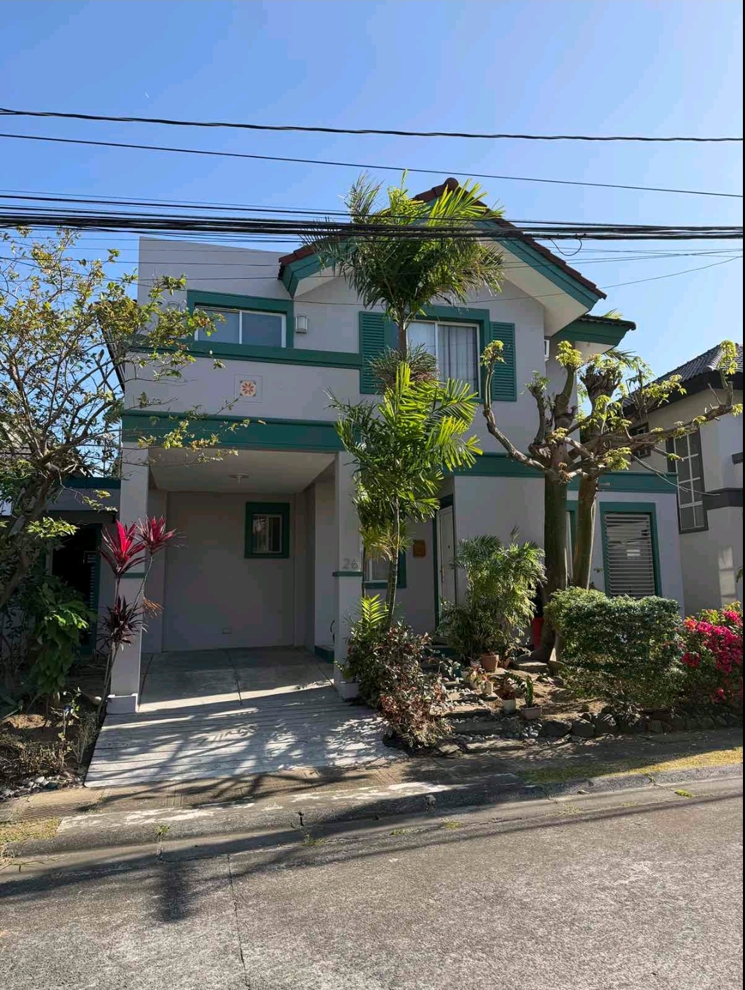 White and green two-storey facade of the Verdana Family Residence with covered carport and tropical front garden
