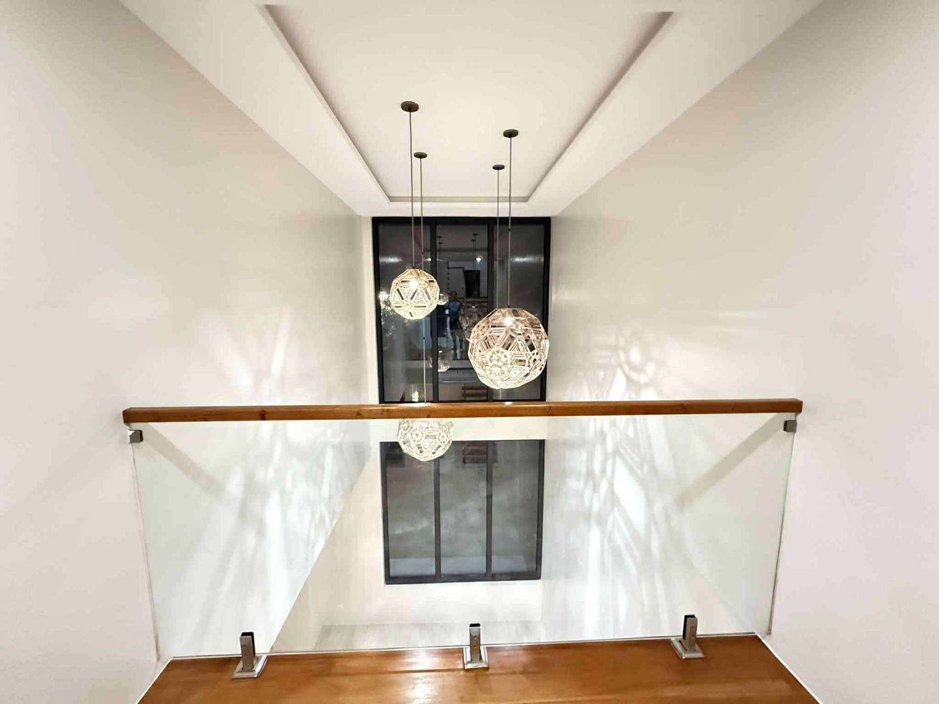 Double-height stairwell with sculptural pendant lights and tall windows