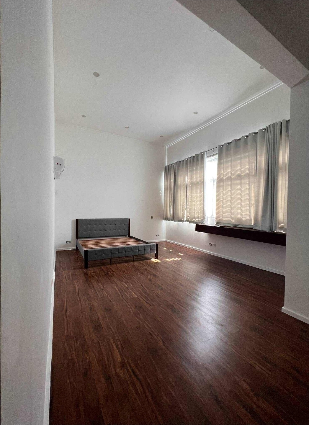 Extra-large master bedroom with dark wood flooring and grey headboard
