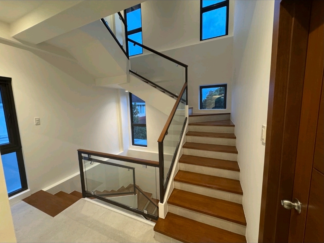 Interior staircase with wood treads, glass panels and wood-capped handrail rising past tall windows