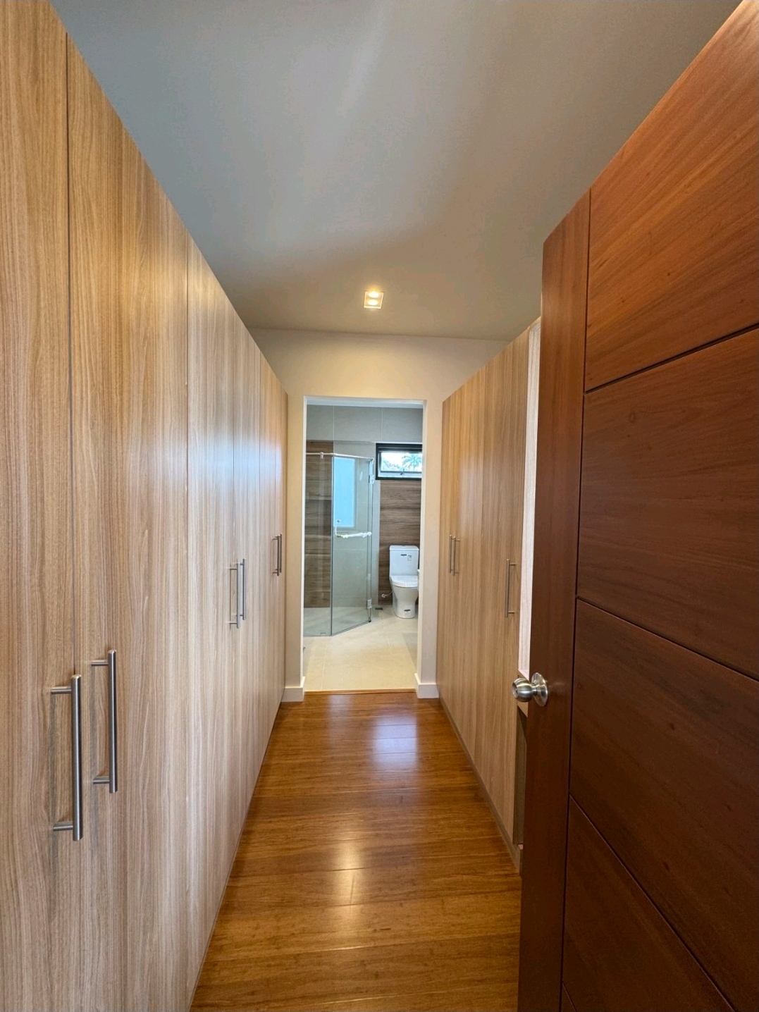 Walk-in closet with floor-to-ceiling wood cabinetry leading to an en-suite bathroom