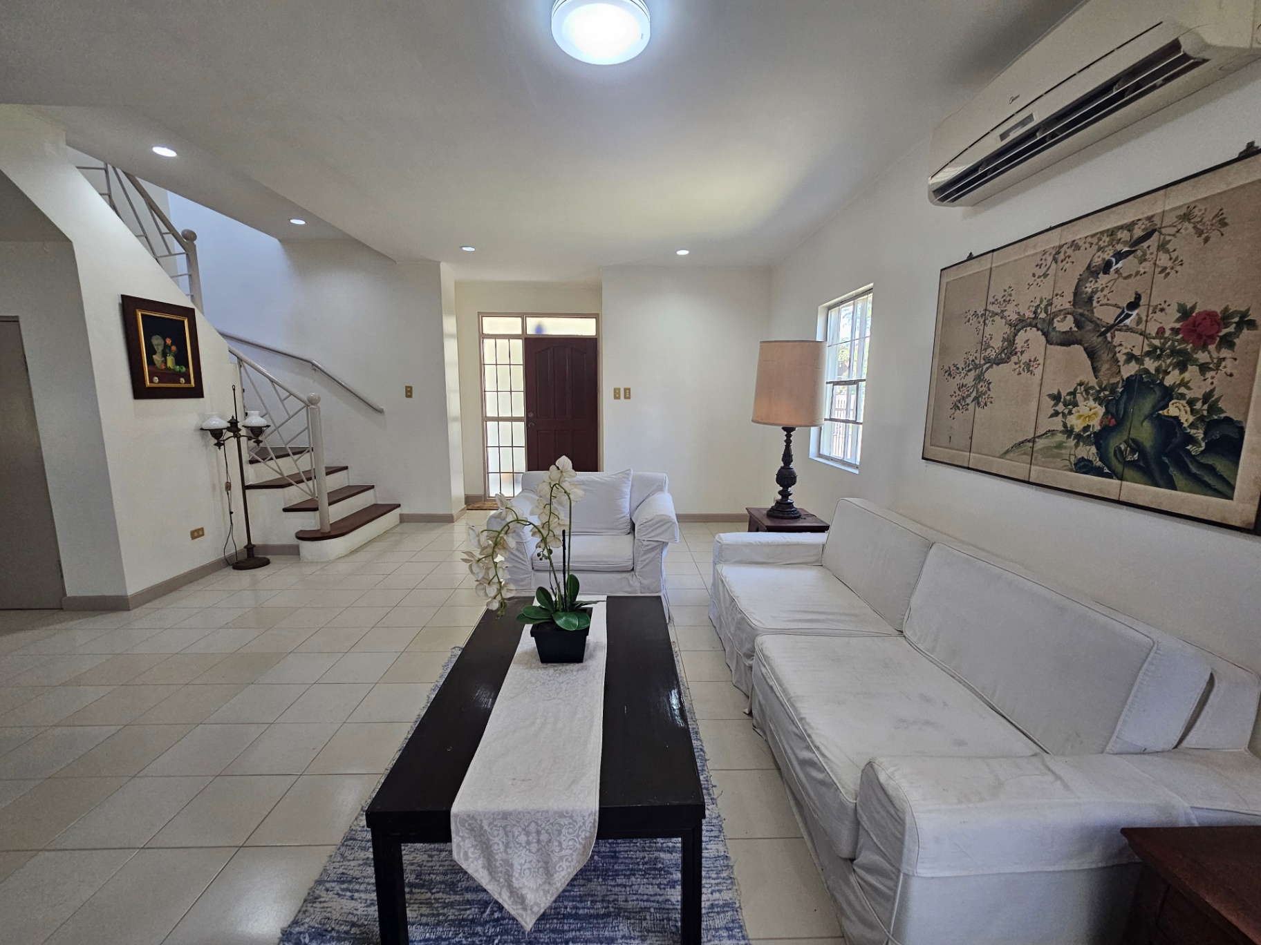Living room with staircase, white sofas, and tiled floors