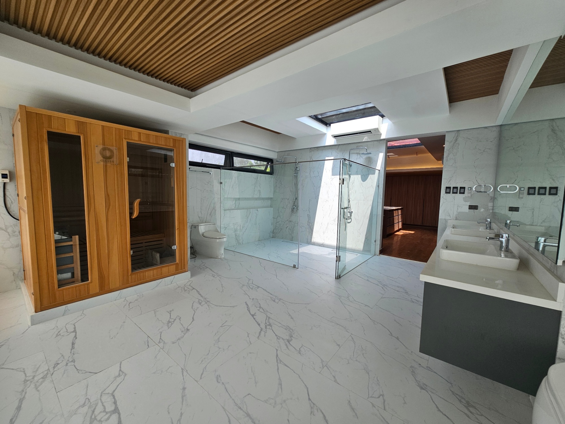 Spa-like marble bathroom with dual vanities, glass shower, and wooden sauna cabin