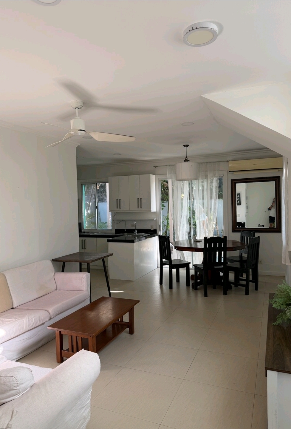 Open-plan living and dining area with white sofas, ceiling fans and view through to the kitchen