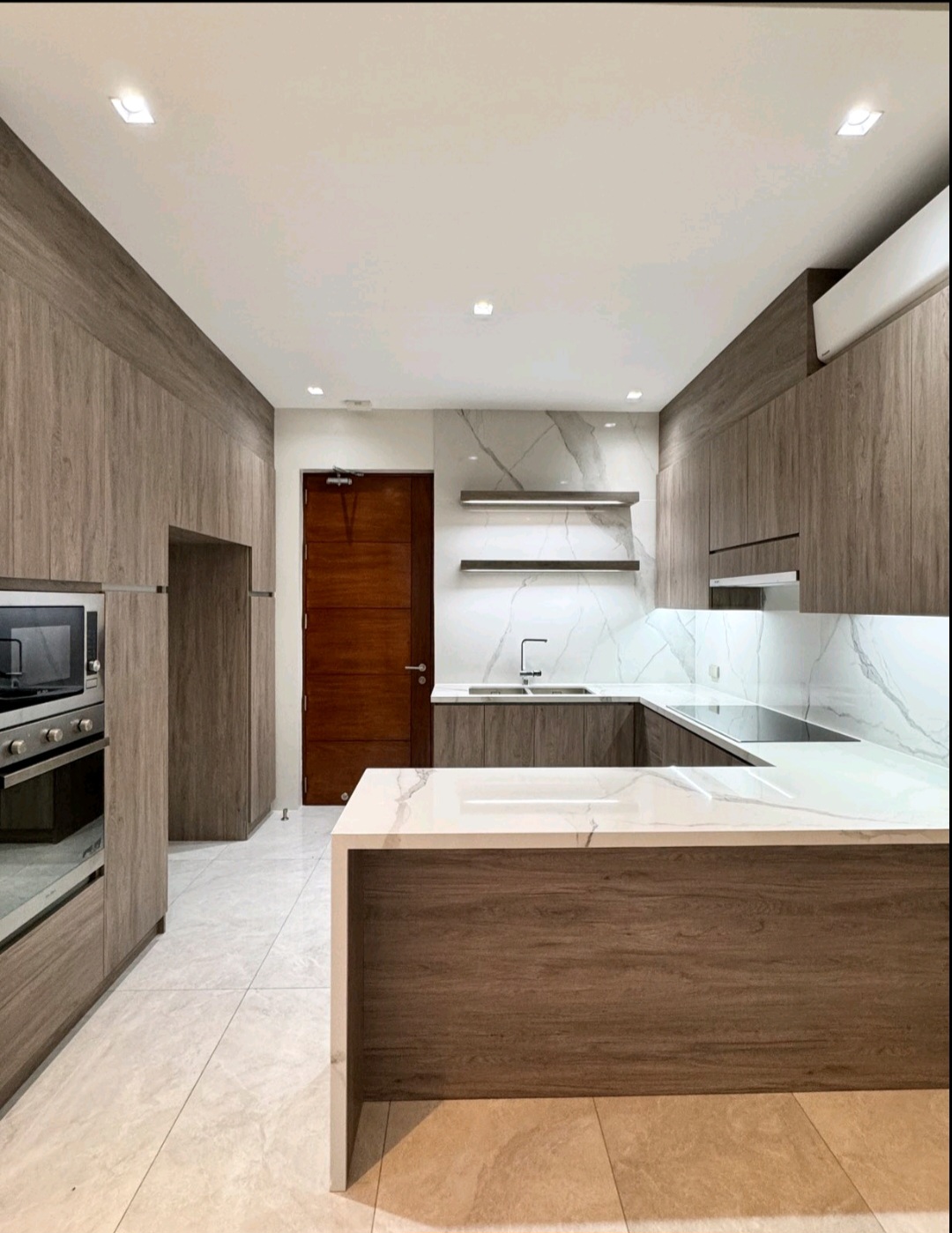 U-shaped modern kitchen with marble countertops, built-in oven, and wood-toned cabinetry