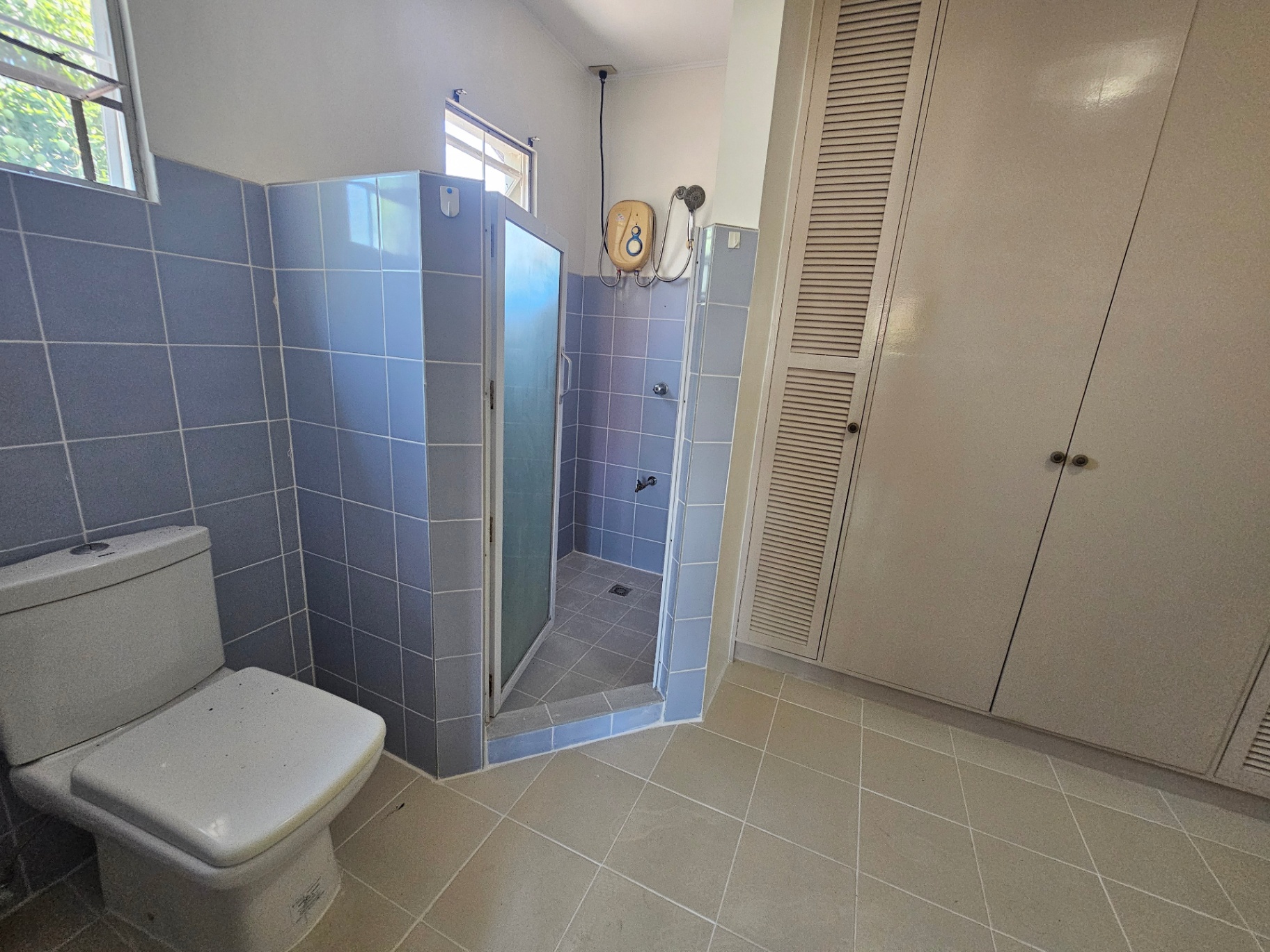 Blue-tiled shower area with water heater and louvered cabinet