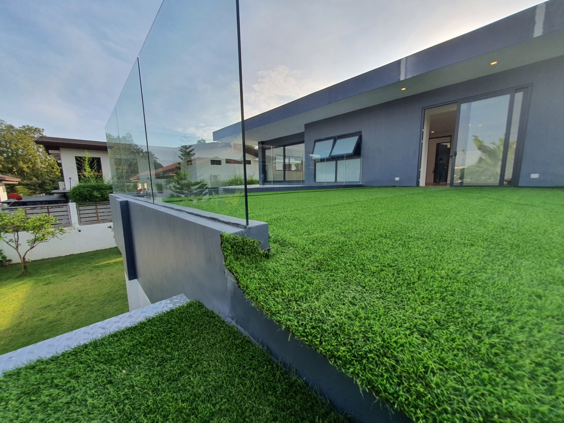 Expansive landscaped lawn with glass railing and mature trees