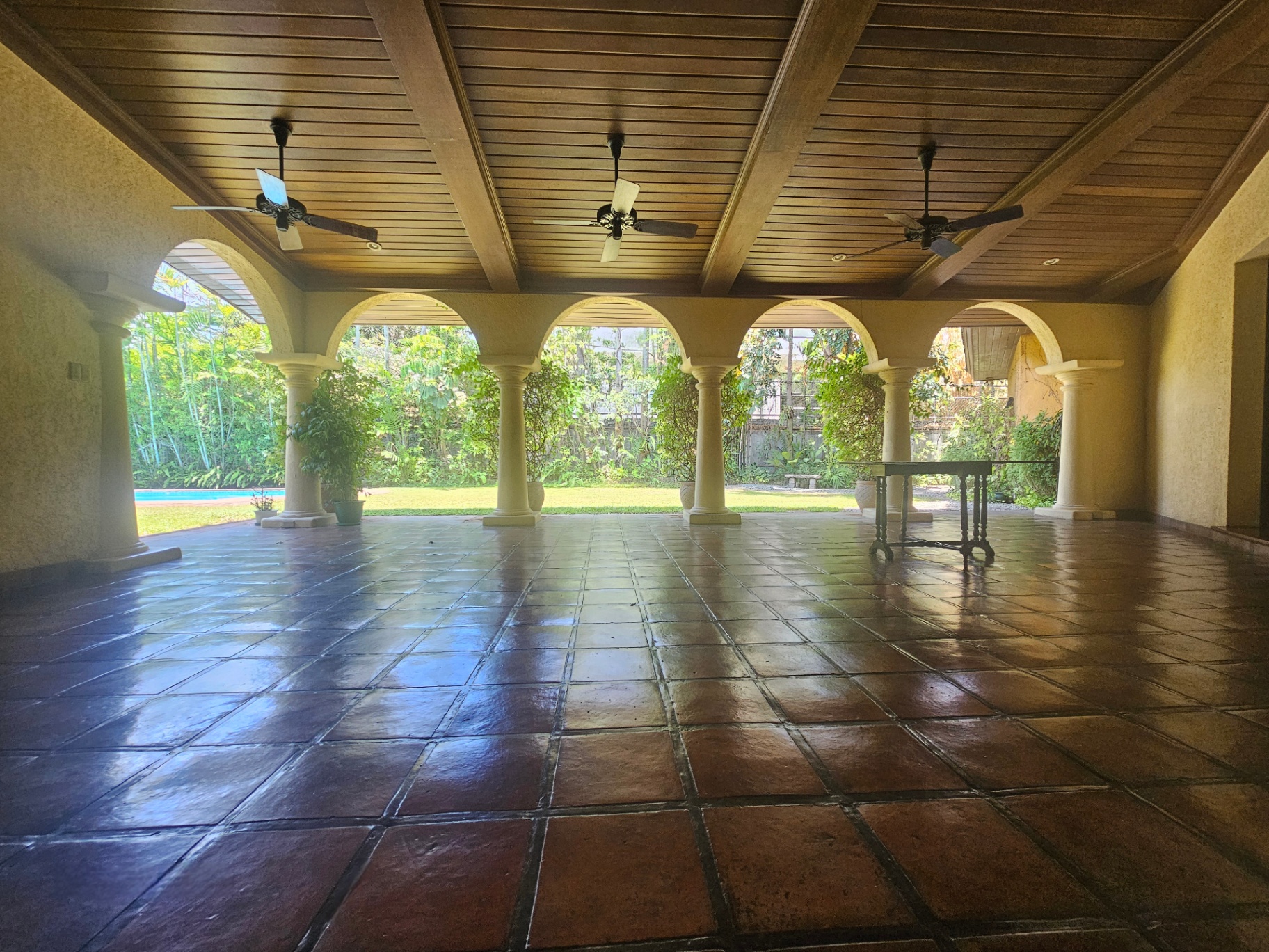 Covered outdoor lanai with timber ceiling, arches, and garden outlook