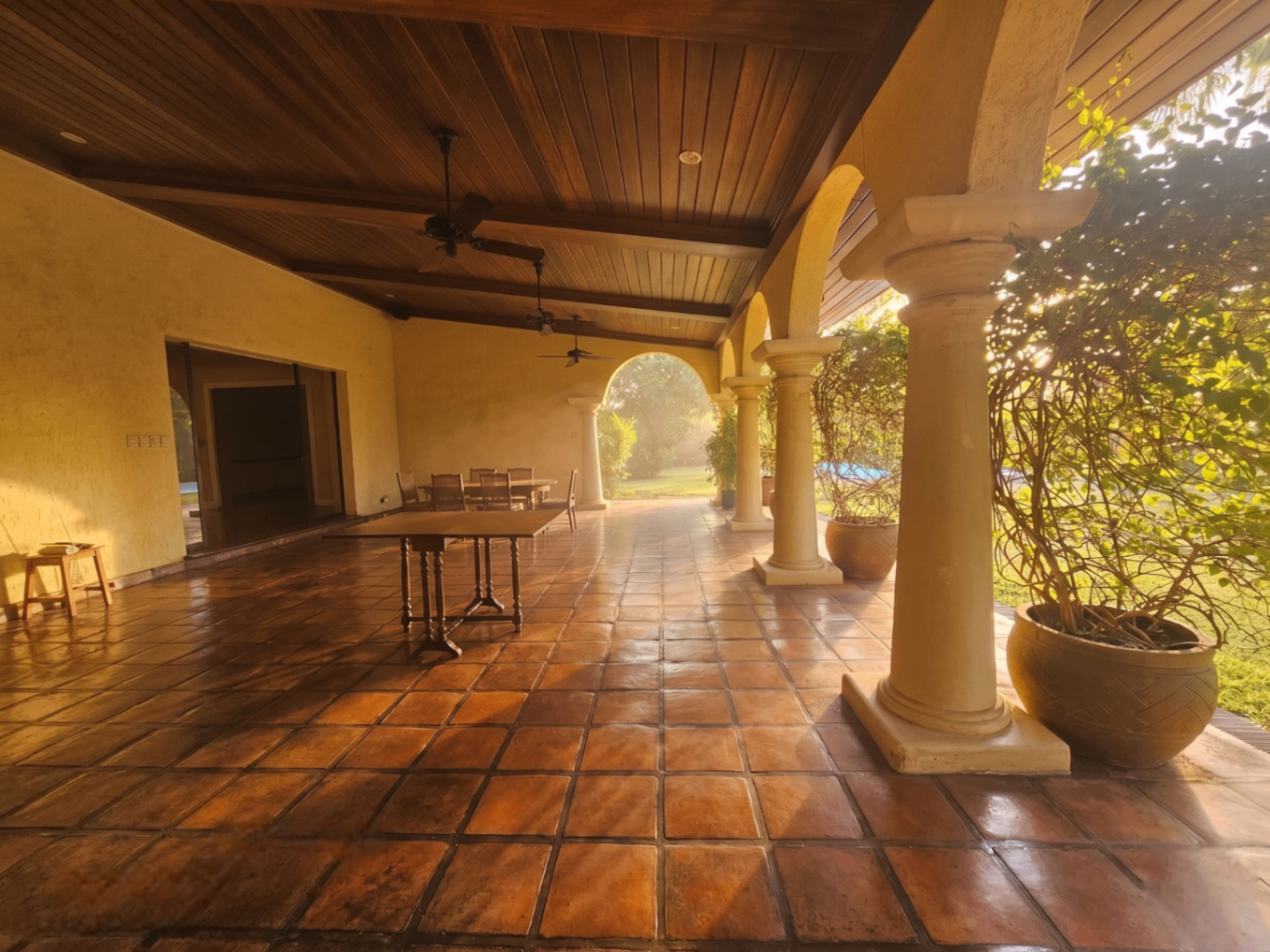 Sunlit lanai with arched columns and outdoor dining setup overlooking the garden