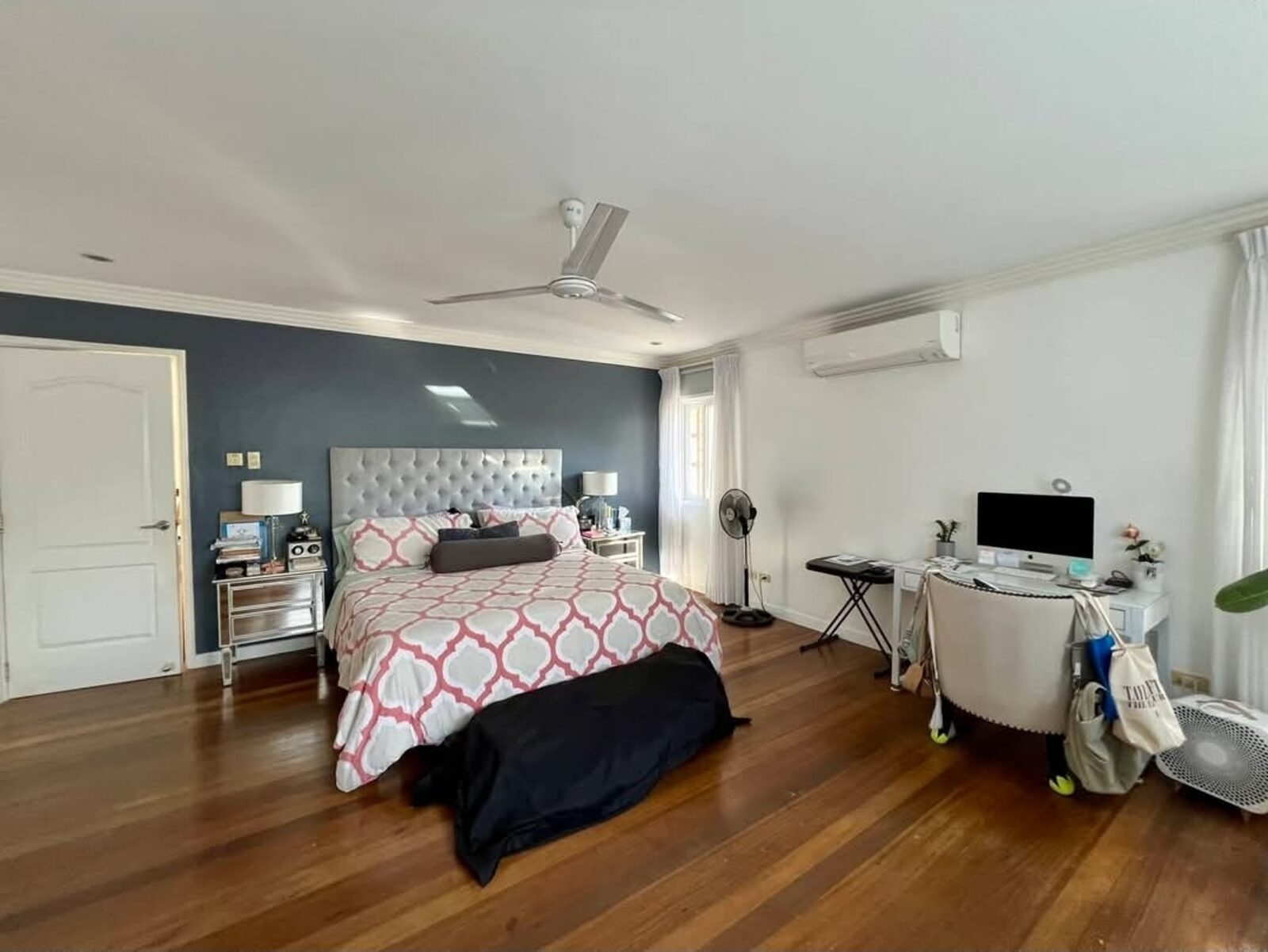 Spacious master bedroom with navy accent wall and hardwood flooring