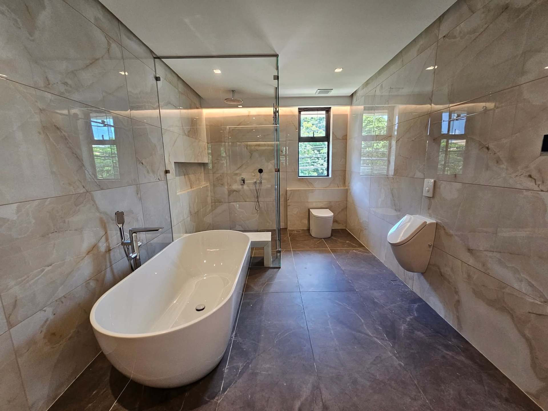 Master bath with marble cladding, freestanding tub and rain shower