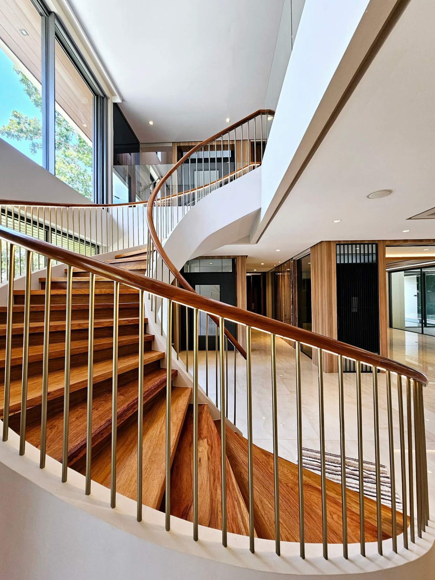 Sweeping curved Narra staircase with brass spindles