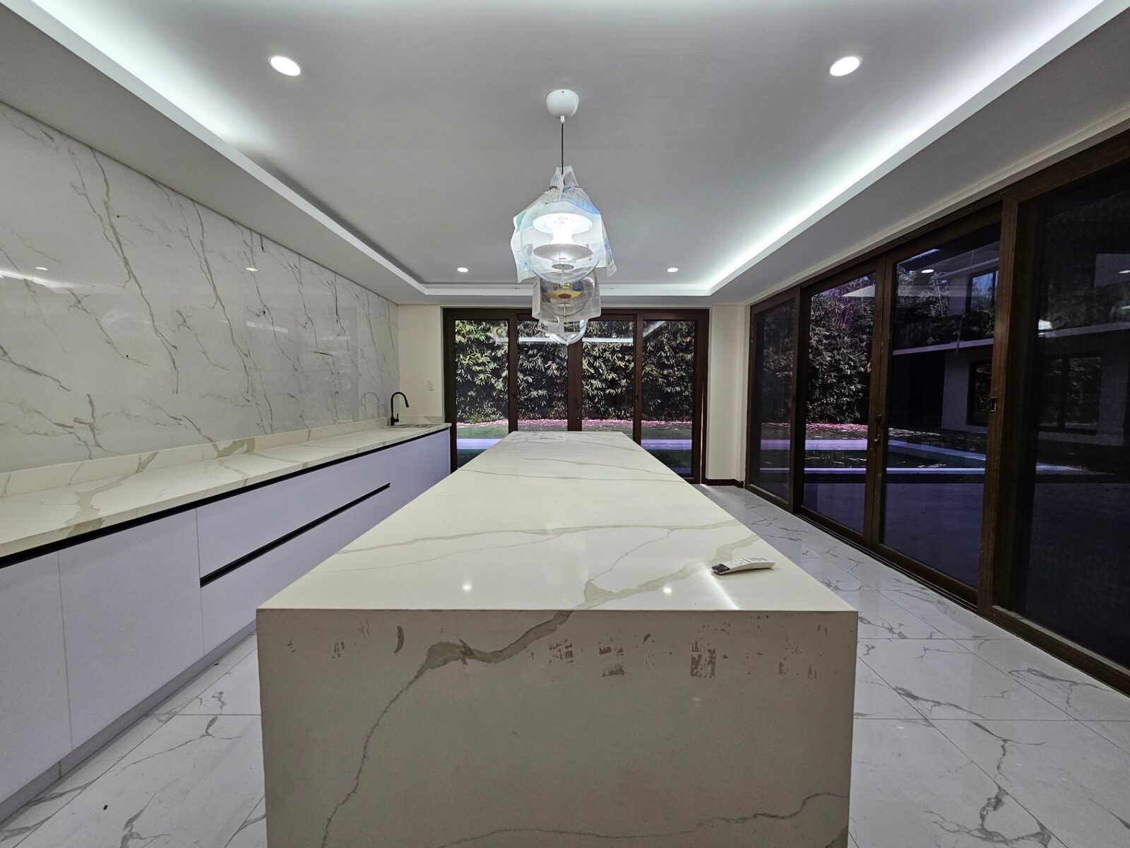 Modern kitchen with long marble waterfall island and garden view