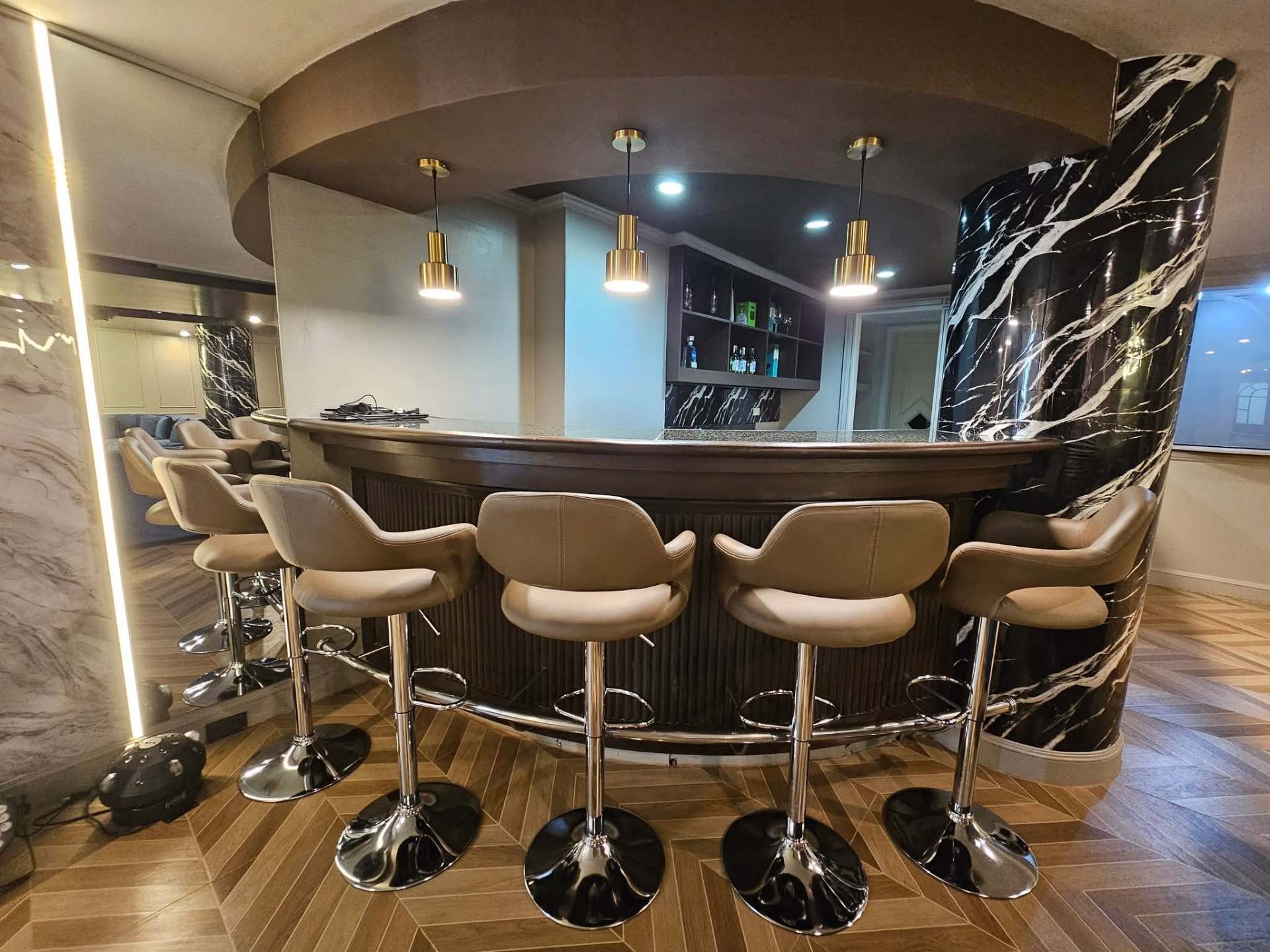Curved private bar with marble column and brass pendant lights