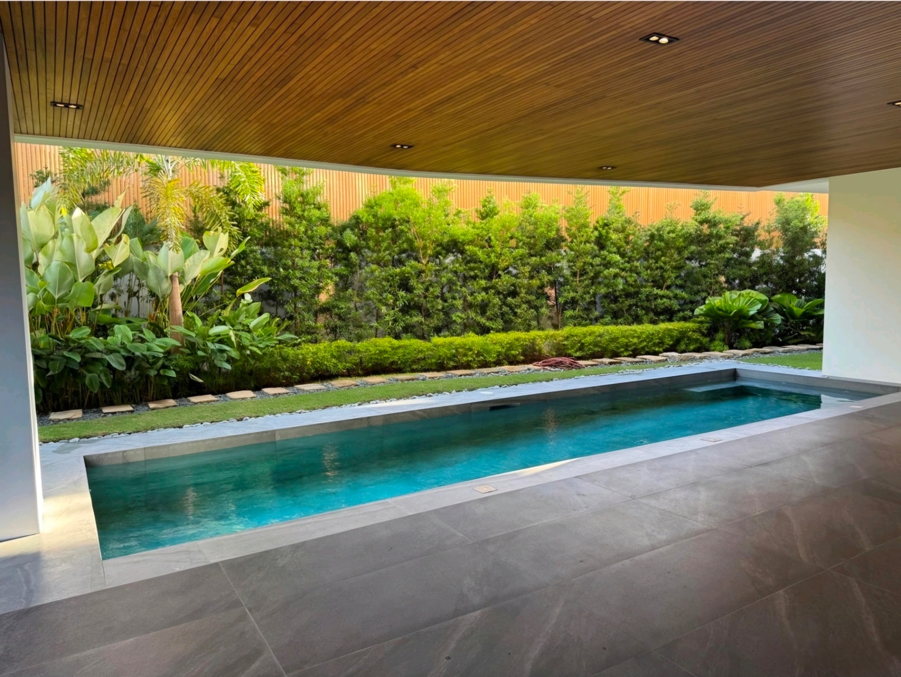 Lap pool framed by tropical landscaped garden and timber-clad lanai