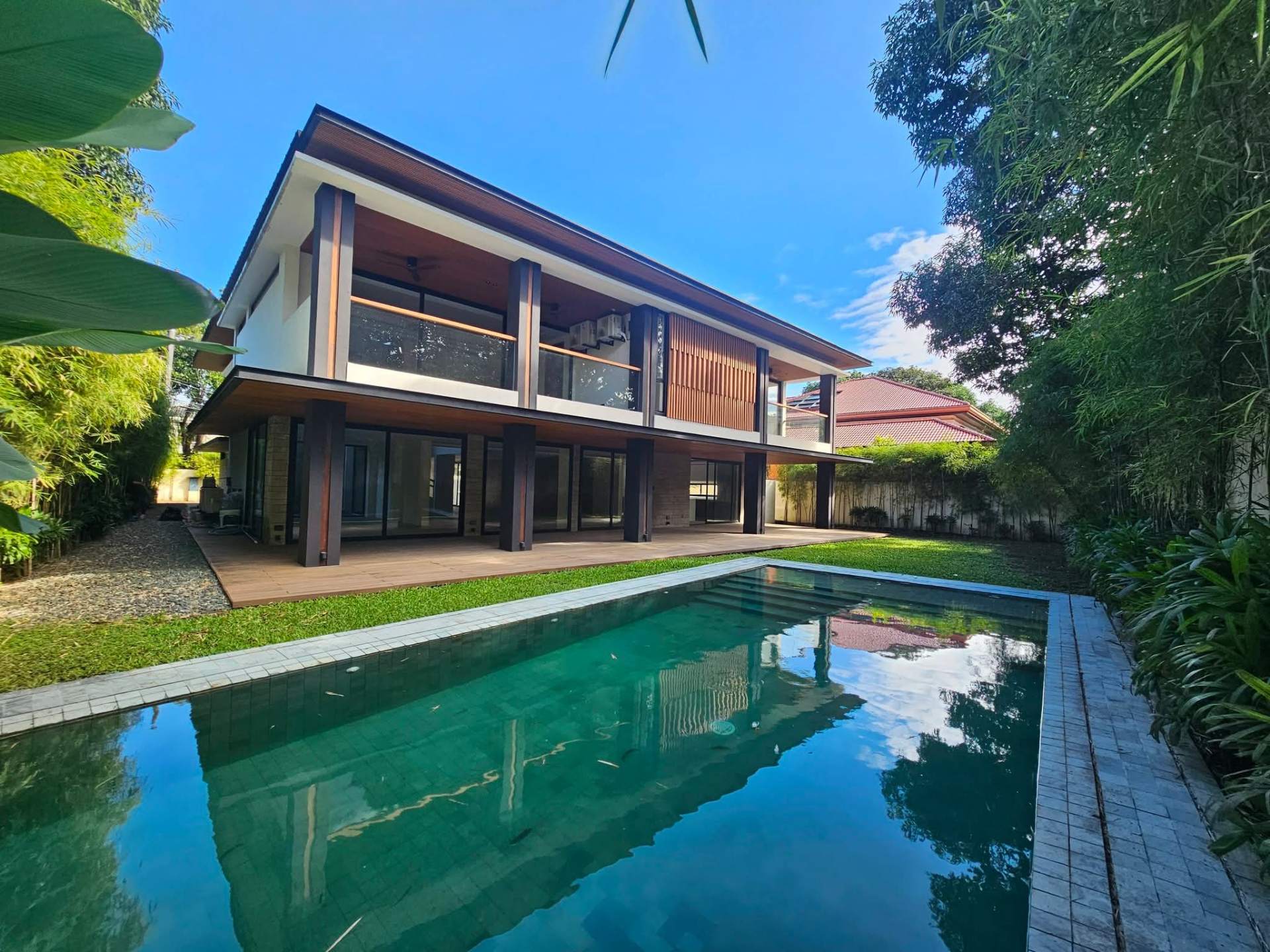 Large rectangular swimming pool framed by lawn and bamboo screen