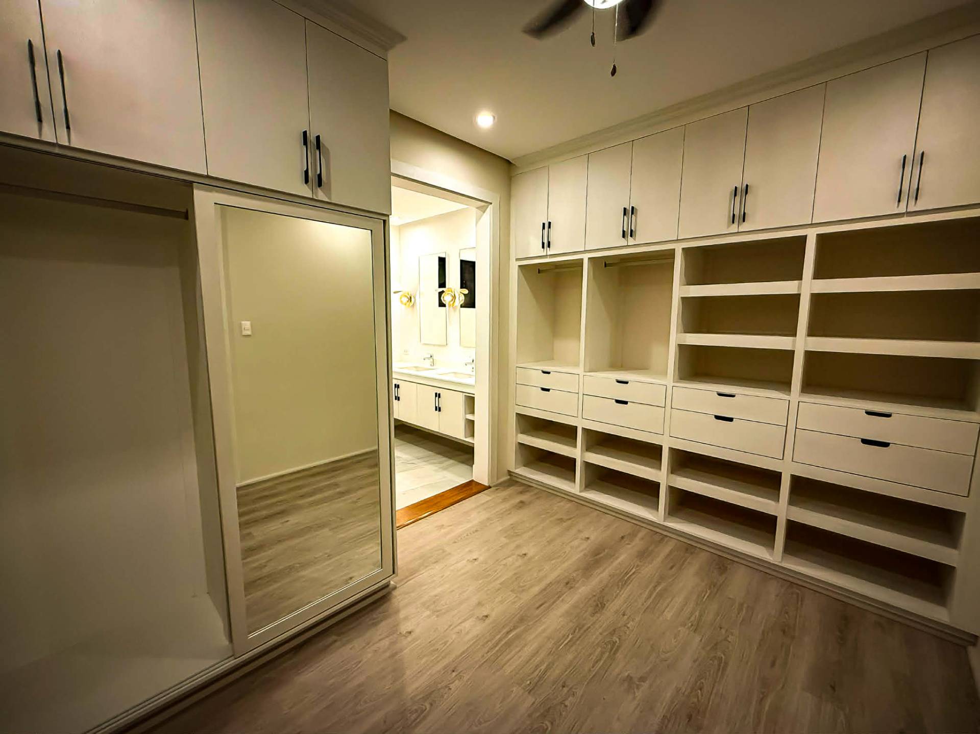 Walk-in closet with custom millwork, full-length mirror, and en-suite bath beyond