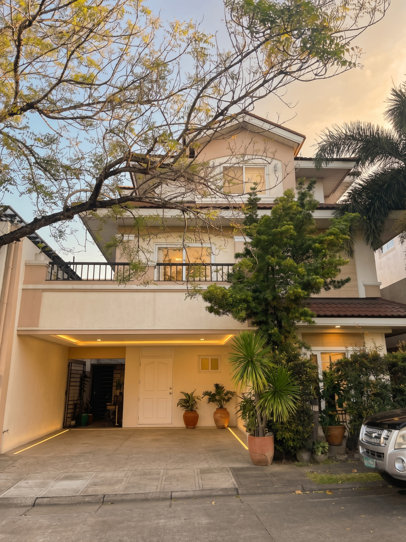 Multi-level facade with mature tree canopy, 2-car carport and warm entry lighting at Verdana Homes Bacoor