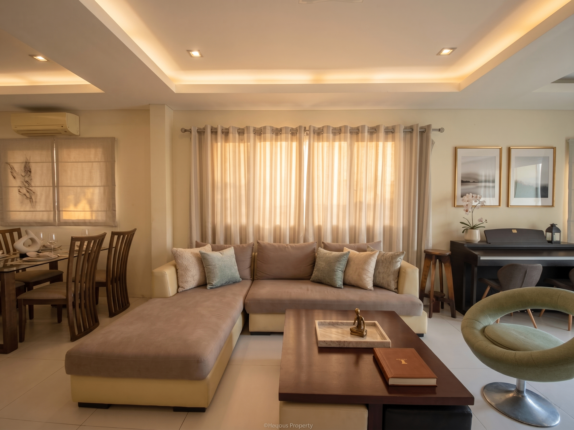 Open living and dining area with cove-lit tray ceiling, sectional sofa and golden-hour light