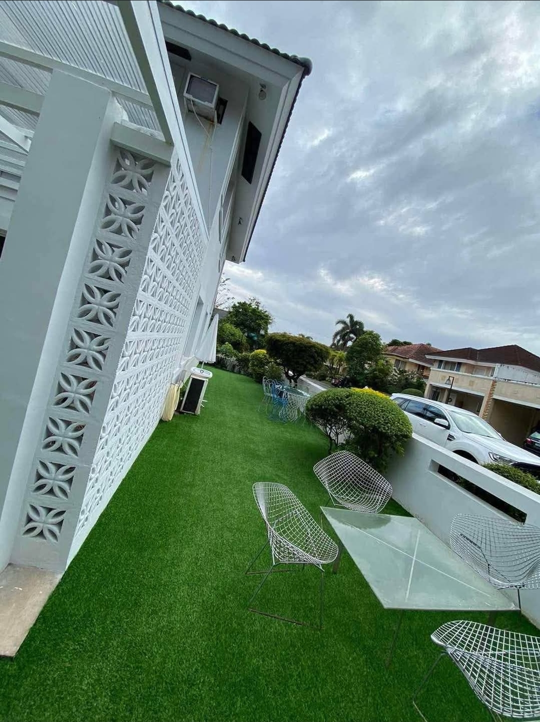 Lawn terrace with breeze-block screen and wire-frame seating overlooking the village