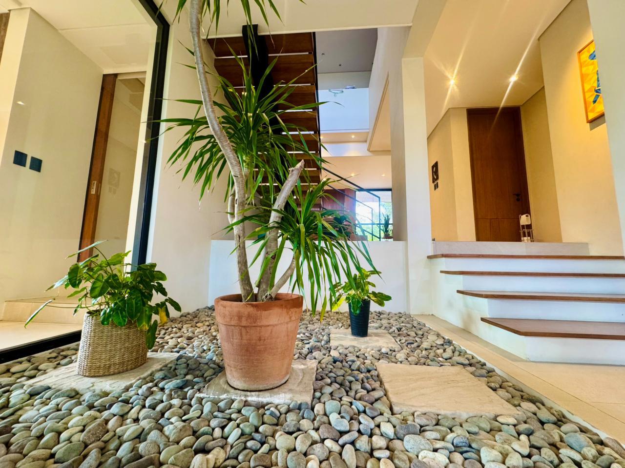 Indoor atrium garden with pebble bed and dracaena, framed by floating wood-tread stairs