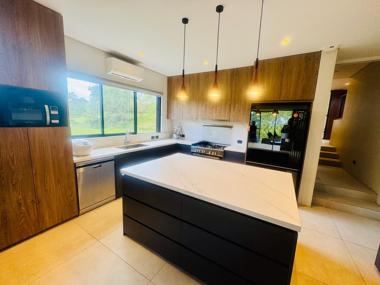 Chef's kitchen with quartz waterfall island, walnut cabinetry, gas range and copper pendants
