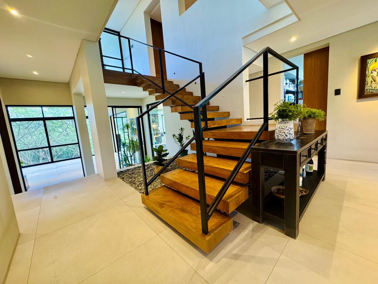 Floating timber stairs with black steel railings rising to the mezzanine over a pebble water feature