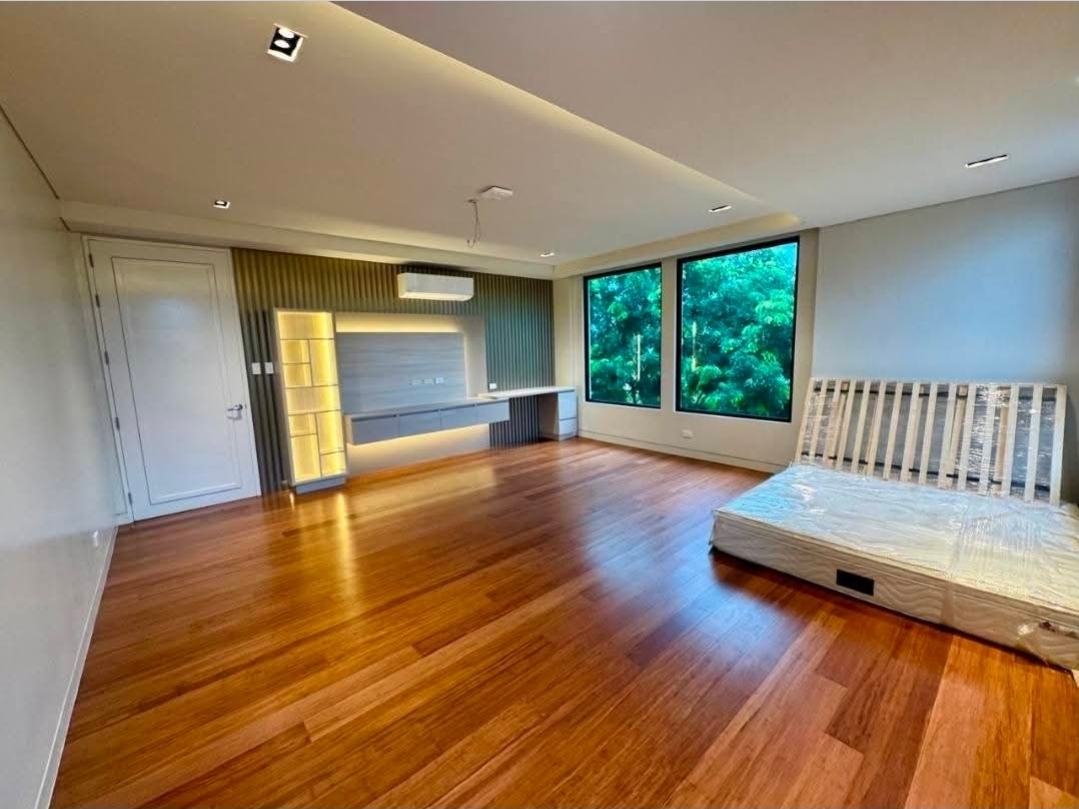 Master bedroom suite with natural wood flooring and forest-view picture window